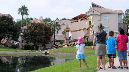 Des passants regardent un h&ocirc;tel partiellement effondr&eacute; &agrave; cause de la formation d'un trou g&eacute;ant. La catastrophe s'est produite, le 11 ao&ucirc;t 2013,&nbsp;&agrave; Clermont, en Floride (Etats-unis), pr&egrave;s du parc d'attractions&nbsp;Disney World. (GERARDO MORA / GETTY IMAGES NORTH AMERICA / AFP)