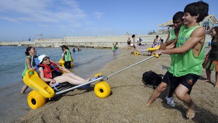 Des jeunes volontaires aident une femme handicap&eacute;e &agrave; prendre un bain de mer, le 29 juillet 2010 sur la plage du Prado &agrave; Marseille, dans le cadre de leur service civique. (ANNE-CHRISTINE POUJOULAT / AFP)