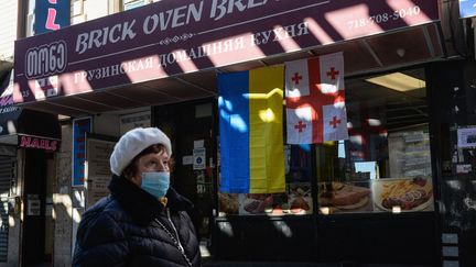 Une femme passe devant une boutique avec des drapeaux ukrainien et géorgien dans une rue de "Little Odessa", un quartier de New York, en mars 2022. (ANGELA WEISS / AFP)