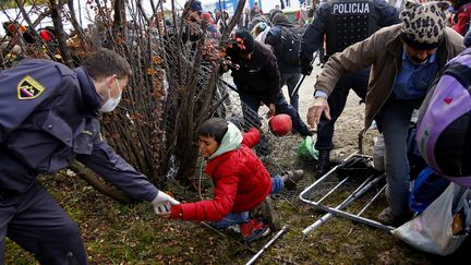 Un policier slov&egrave;ne aide un enfant &agrave; se relever tandis qu'une foule tente de briser le cordon de police &agrave; Sentj, en Slov&eacute;nie, le 20 octobre 2015. (? LEONHARD FOEGER / REUTERS / X00360)