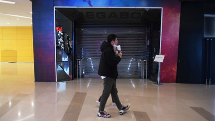 Un couple marche devant le cinéma Megabox fermé à Pékin, en Chine, le 16 février 2020. L'établissement aux huit écrans est fermé depuis près d'un mois à cause de la crise du coronavirus. (GREG BAKER / AFP)