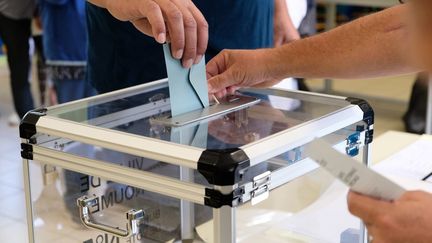 Une personne glisse son bulletin dans un bureau de vote, le 4 octobre 2020. (THEO ROUBY / AFP)