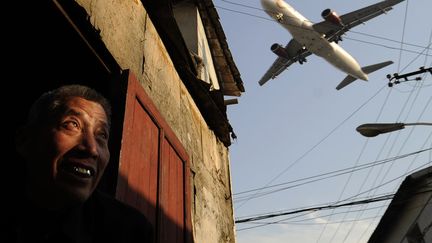 Un homme regarde un avion voler au-dessus de la maison pr&egrave;s de l'a&eacute;roport de Shanghai (Chine), le 5 janvier 2012. (PETER PARKS / AFP)