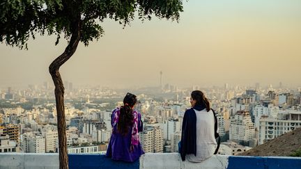 Des femmes iraniennes ne portant pas le hijab obligatoire sont assises sur le Bam-e Tehran (toit de Téhéran), qui surplombe la ville de Téhéran. (SASAN / MIDDLE EAST IMAGES / AFP)