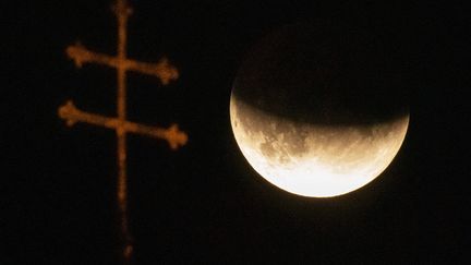 A Munich (Allemagne), l'éclipse partielle de lune est immortalisée à côté de la croix d'une église, mardi 16 juillet 2019.&nbsp; (PETER KNEFFEL / DPA / AFP)