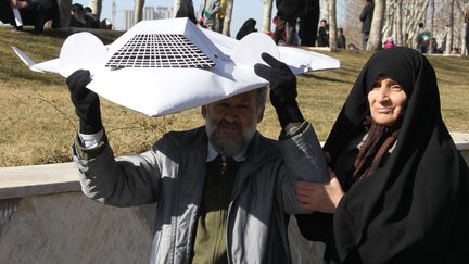 Un couple brandit une r&eacute;plique miniature du drone RQ-170 am&eacute;ricain que l'Iran dit avoir captur&eacute;, le 11 f&eacute;vrier 2012 &agrave; T&eacute;h&eacute;ran. (ATTA KENARE / AFP)