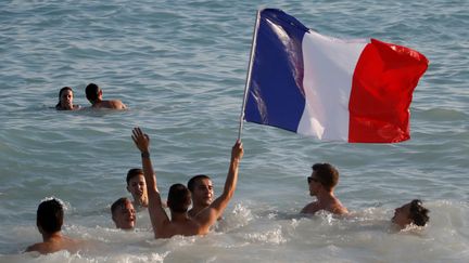 Pour mieux reprendre ses esprits, rien de tel qu'un bain improvisé à la Méditerranée, mais sans lâcher son drapeau, sur la plage de Nice. (ERIC GAILLARD / REUTERS)