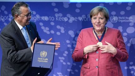 La chancelière allemande Angela Merkel reçoit une médaille de Tedros Adhanom Ghebreyesus, directeur général de l'OMS, lors de la cérémonie d'inauguration du centre de recherche et détection des épidémies à Berlin, le 1er septembre 2021. (MICHAEL SOHN / AP / AFP)