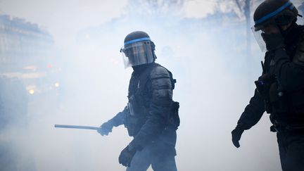 Un policier tenant une matraque à la main entouré de fumée de gaz lacrymogène lors d'une manifestation à Paris, le 30 janvier 2021. (CHRISTOPHE ARCHAMBAULT / AFP)