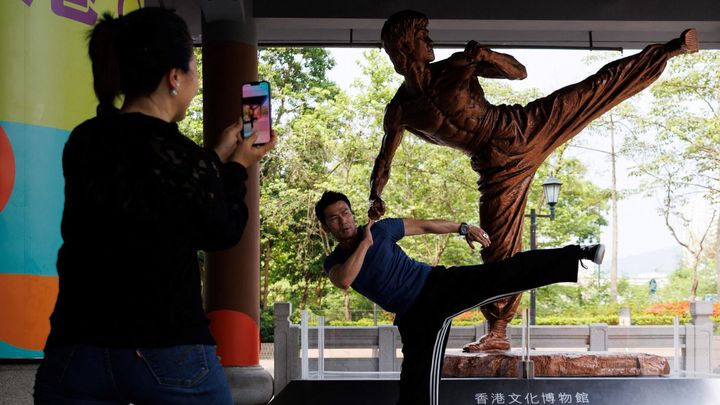Des visiteurs prennent des photos d'une statue de Bruce Lee à l'extérieur du Hong Kong Heritage Museum à Hong Kong, avant le 50e anniversaire de la mort de la star des arts martiaux, le 20 juillet 2023 (May JAMES / AFP)