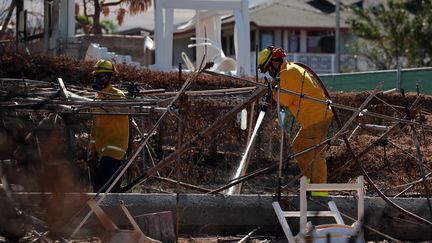 Des pompiers s'activent dans les restes d'une habitation détruite par un incendie qui a ravagé la ville touristique de Lahaina, à Hawaï, le 22 août 2023. (HIROTO SEKIGUCHI / YOMIURI / AFP)