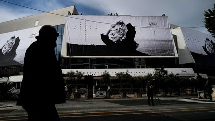 Des ouvriers installent l'affiche officielle de la 76e édition du Festival de Cannes- une photographie de l'actrice Catherine Deneuve par  Jack Garofalo - sur la façade du Palais des Festivals à Cannes, le 14 mai 2023. (VALERY HACHE / AFP)