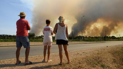 Des vacanciers observent un feu de forêt, le 18 août 2021, à La Garde-Freinet (Var). (NICOLAS TUCAT / AFP)