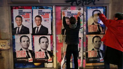 Un militant soutient à l'ancien Premier ministre et candidat à la primaire de la gauche Manuel Valls, colle une affiche sur celle d'un autre candidat de la gauche Benoit Hamon. Paris, le 11 janvier 2017. (JACQUES DEMARTHON / AFP)