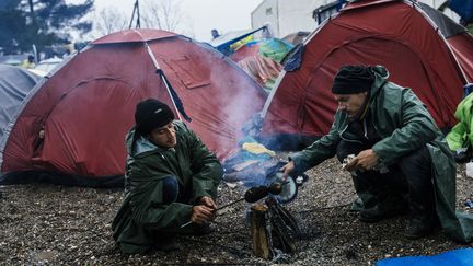 Deux hommes font cuire des pommes de terre sur un réchaud improvisé, le 9 mars 2016. Une épicerie s'est ouverte sur le camp mais les denrées restent chères.&nbsp; (DIMITAR DILKOFF / AFP)