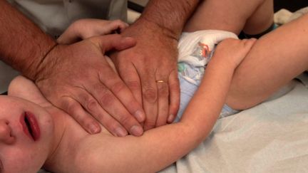 Un kinésithérapeute masse la cage thoracique d'un bébé atteint d'une bronchiolite. (CHRISTIAN LANTENOIS / MAXPPP)