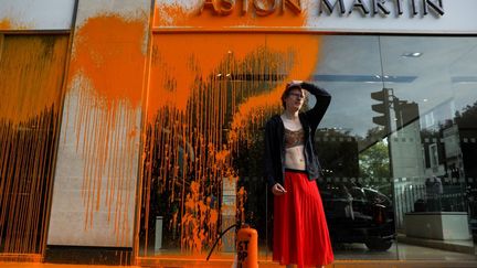 Un militant écologiste du groupe Just Stop Oil vient de pulvériser de la peinture orange sur la vitrine d'une&nbsp;concession Aston Martin, dans le centre de Londres, le 16 octobre 2022. (ISABEL INFANTES / AFP)