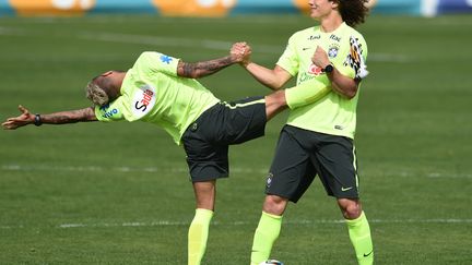 Le d&eacute;fenseur br&eacute;silien David Luiz (D) aide son compatriote Dani Alves &agrave; s'&eacute;tirer lors d'un entra&icirc;nement de l'&eacute;quipe nationale &agrave; Teresopolis (Br&eacute;sil), le 7 juillet 2014. (VANDERLEI ALMEIDA / AFP)