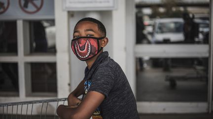 Un garçon, appuyé sur son caddie et arborant un masque, fait&nbsp;la queue devant un magasin Makro de Soweto, à Johannesburg (Afrique du Sud), le 24 mars 2020, au lendemain de l'annonce d'un confinement par le président sud-africain&nbsp;Cyril Ramaphosa. (MARCO LONGARI / AFP)