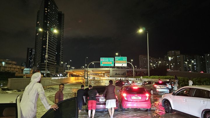 Dubai residents find themselves forced to get out of their cars on a flooded road following heavy rains in the United Arab Emirates, April 16, 2024. (STRINGER / ANADOLU / AFP)