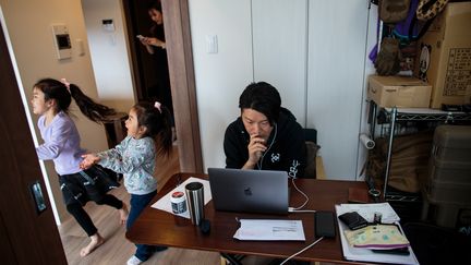 Un homme télétravaille chez lui pendant que ses enfants jouent, à Tokyo, le 23 mars 2020. (BEHROUZ MEHRI / AFP)