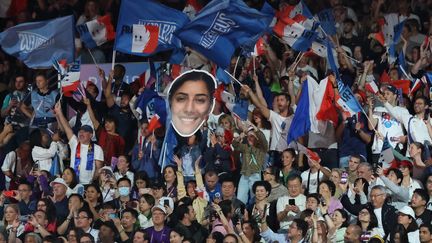 Des supporters de l'équipe de France brandissent des drapeaux et une photo de Shirine Boukli dans les tribunes de l'Arena Champ-de-Mars, aux JO de Paris, le 27 juillet 2024. (JACK GUEZ / AFP)