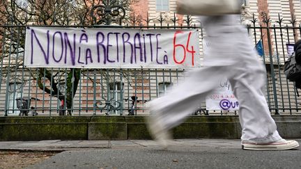 Une personne passe devant une banderole accrochée à la clôture du lycée Zola, sur laquelle on peut lire "Non à la retraite à 64 ans", à Rennes, le 19 janvier 2023. (DAMIEN MEYER / AFP)