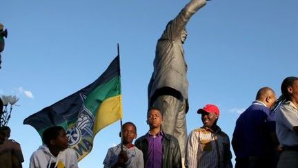 Des partisans de l'ANC brandissant un drapeau de leur parti devant une statue de Mandela. Cape Town. 9 décembre 2013. (AFP/ Jennifer Bruce)