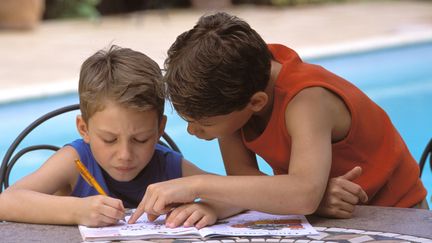 Deux petits garçons remplissent leurs cahiers de vacances au bord d'une piscine. (TILL JACKET / PHOTONONSTOP via AFP)