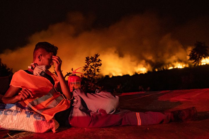 Un volontaire se repose alors que les flammes s'élèvent d'une forêt qui brûle en arrière-plan près d'Akcayaka, une ville de la province de Mugla (Turquie), le 6 août 2021. (YASIN AKGUL / AFP)