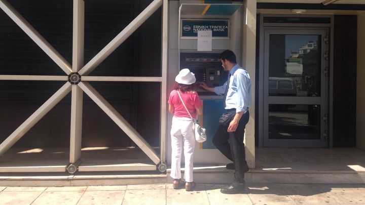 Un employ&eacute; de la Banque nationale de Gr&egrave;ce aide une femme &agrave; retirer de l'argent &agrave; un distributeur d'Ath&egrave;nes, le 14 juillet 2015. (ARIANE NICOLAS / FRANCETV INFO)