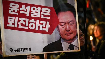 Une pancarte brandie lors d'une manifestation à Séoul (Corée du Sud), le 4 décembre 2024, contre le président sud-coréen, avec l'inscription "Yoon Suk-yeol devrait se retirer". (PHILIP FONG / AFP)