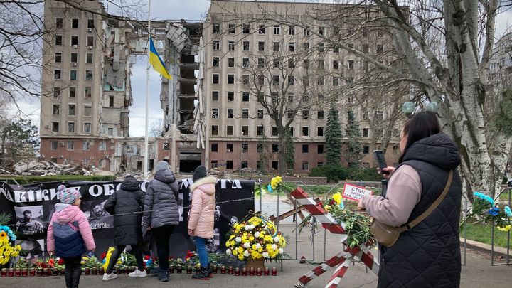 Les habitants de Mykolaïv (Ukraine) se recueillent, le 29 mars 2023, devant le siège de l'administration régionale, visée par une frappe il y a un an. (MATHIEU DREUJOU / FRANCE TELEVISIONS)