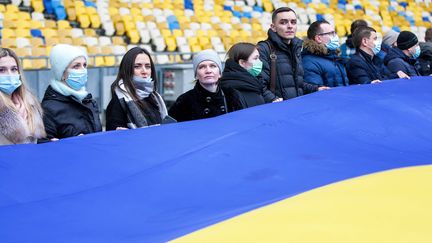 Des Ukrainiens déroulent un très long drapeau dans un stade de Kiev pour célébrer le "jour de l'unité" dans le pays, le 16 février 2022. (PAVLO GONCHAR / ZUMA PRESS / MAXPPP)