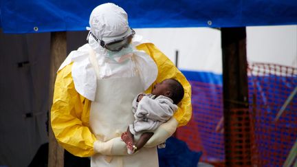 Un m&eacute;decin en tenue de protection contre Ebola tient dans ses bras un b&eacute;b&eacute; de deux semaines &agrave;&nbsp;Gueckedou (Guin&eacute;e), le 16 octobre 2014.&nbsp; (KRISTIN PALITZA / DPA / AFP)