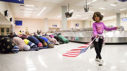 Une jeune fille danse avec un drapeau américain pendant que des femmes prient contre le décret anti-immigration, à l'aéroport de Dalls, dimanche 29 janvier 2017. (LAURA BUCKMAN / REUTERS)