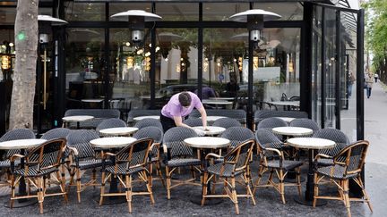 Un serveur nettoie les tables de la terrasse de son café en prévision de la levée des restrictions liées au Covid-19, mardi 11 mai 2021 à Paris. (LUDOVIC MARIN / AFP)