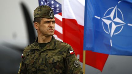 Un soldat polonais se tient devant des drapeaux am&eacute;ricains, polonais et de l'Otan, &agrave; Swidwin (Pologne),&nbsp;lors de l'arriv&eacute;e de 150 soldats am&eacute;ricains pour des exercices militaires en Pologne et dans les pays baltes, le 23 avril 2014. (KACPER PEMPEL / REUTERS)