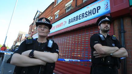 Des policiers devant un barbier, perquisitionné dans le cadre de l'enquête sur l'attentat de la Manchester Arena, le 26 mai 2017, dans le quartier de Moss Side à Manchester. (LINDSEY PARNABY / AFP)