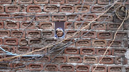 Une femme regarde par la fen&ecirc;tre de sa maison de briques situ&eacute; dans un vieux quartier de Delhi (Inde), le 15 mai 2013. (MANSI THAPLIYAL / REUTERS)