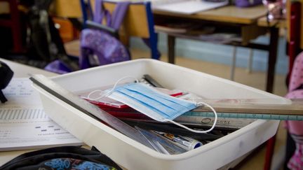 Un masque chirurgical est rangé dans une boîte avec des affaires scolaires, dans une école&nbsp;élémentaire des Hautes-Alpes, le 25 février 2022. (THIBAUT DURAND / HANS LUCAS / AFP)