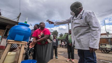 Le Dr Fredrick Ochenge prend la température d'une femme&nbsp;à un des&nbsp;points d'eau collectif, installés dans les rues pour permettre aux habitants de se laver régulièrement les mains. (DONWILSON ODHIAMBO / SOPA IMAGES / SIPA)