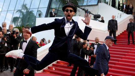 L'artiste Jr fait le pitre sur le tapis rouge ! Avec ses fidèles lunettes de soleil sur le bout du nez, il porte un costume en velours bleus et des baskets blanches pour un look chic et décontracté.&nbsp; (VALERY HACHE / AFP)