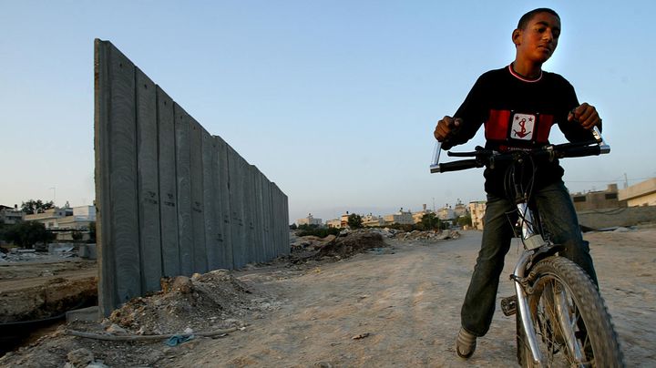 Un jeune Palestinien fait du v&eacute;lo &agrave;&nbsp;Nazlat Issa,&nbsp;pr&egrave;s d'une partie du mur qui s&eacute;pare Isra&euml;l et la Cisjordanie, le 25 novembre 2003. (YOAV LEMMER / AFP)