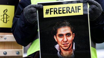 Un membre d'Amnesty International tient la photo du militant saoudien Raif Badawai emprisonné dans son pays, lors d'un rassemblement devant l'ambassade de l'Arabie saoudite à Bruxelles (Belgique), le 8 janvier 2021. (KENZO TRIBOUILLARD / AFP)