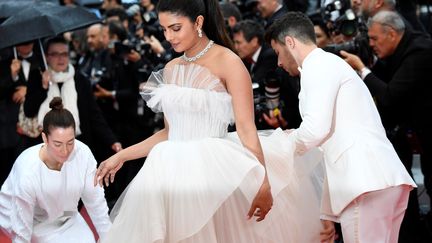 La chanteur américain Nick Jonas aide l'actrice indienne Priyanka Chopra avec sa longue robe de tulle blanc. (CHRISTOPHE SIMON / AFP)