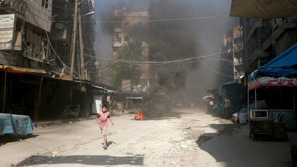 Un enfant court dans une rue d'Alep, devant un pneu incendié dans le but d'empêcher les bombardements, dimanche 31 juillet. (BEHA EL HALEBI / ANADOLU AGENCY / AFP)