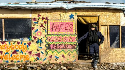 Un policier&nbsp;se tient devant un restaurant installé dans la "jungle" de Calais (Pas-de-Calais), le 3 mars 2016. (PHILIPPE HUGUEN / AFP)