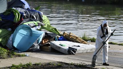 Un ouvrier nettoie des migrants du "Millénaire" le long du canal de Saint-Denis près de la porte de la Villette, au nord de Paris, suite à son évacuation le 30 mai 2018. (GERARD JULIEN / AFP)