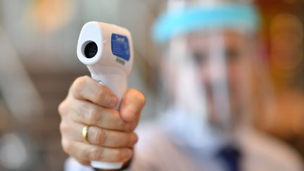 Un membre du personnel portant un écran facial utilise un thermomètre laser pour tester les températures des clients dans un magasin Furniture Village à Croydon, dans le sud-est de Londres le 5 juin 2020. (BEN STANSALL / AFP)